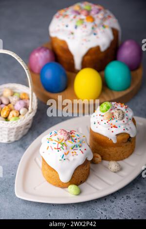 Zwei kleine Osterkulichs mit kandierten Früchten in weißer Glasur mit bunten Streuseln im Schnitt. Bemaltes Hühnchen und Wachteleier. Traditionelle Osterbak Stockfoto