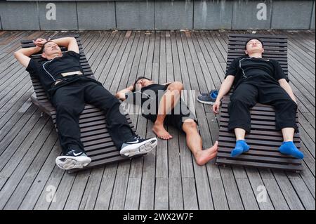 29.07.2018, Singapur, Republik Singapur, Asien - eine Gruppe von Männern macht ein Nickerchen auf hölzernen Liegestühlen an der Uferpromenade in Marina Bay. Stockfoto