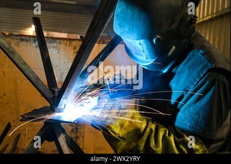 Schweißer bei der Arbeit. Funkeln beim Schweißen. Männlicher Arbeiter mit Helm und Handschuhen. Schweißen von Metall im Werk. Nahaufnahme des Industriearbeiters auf der Baustelle. Stockfoto