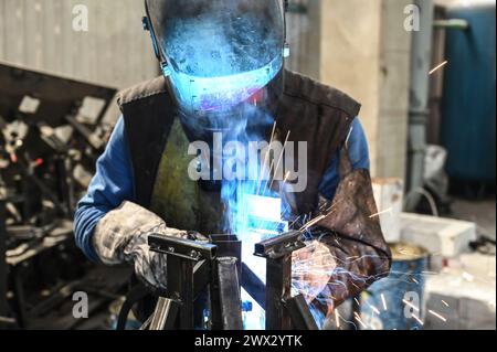 Schweißer bei der Arbeit. Funkeln beim Schweißen. Männlicher Arbeiter mit Helm und Handschuhen. Schweißen von Metall im Werk. Nahaufnahme des Industriearbeiters auf der Baustelle. Stockfoto