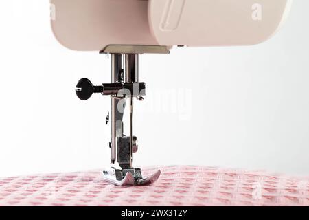 Eine Nadel mit Nadelhalter und Nähmaschinenfuß auf einem Hintergrund aus rosa Stoff. Makro, Industrie. Kopierbereich für Text Stockfoto