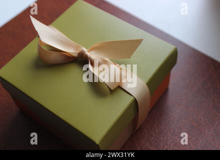 Geschenkverpackung in Olivtönen mit elegantem beigefarbenem Band auf braunem Leder Stockfoto