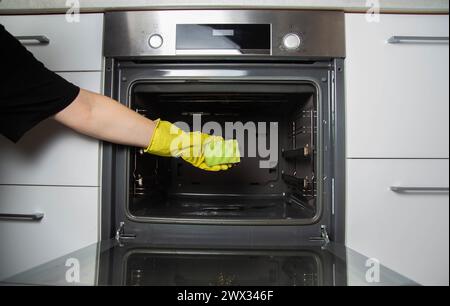 Ein Mädchen hält einen Schwamm in der Hand vor dem Hintergrund eines Ofens. Konzept zur Reinigung von Elektroöfen in der Küche. Reinigungsfirma Stockfoto