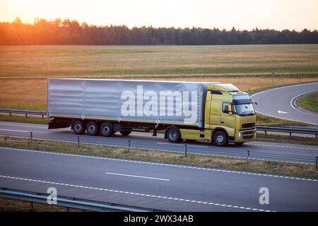 Ein Lkw mit Kippauflieger transportiert abends vor dem Hintergrund eines Sommersonnenverganges Fracht auf der Autobahn. Das Konzept des Frachttranspors Stockfoto