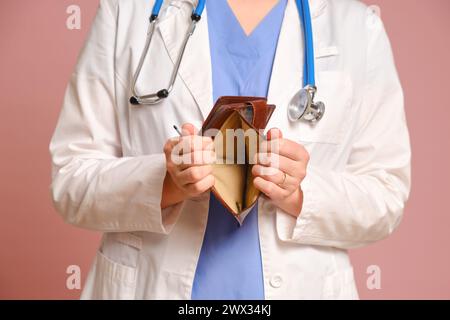 Eine Ärztin, die eine leere Brieftasche in den Händen hält, rosa Hintergrund des Studios. Krankenschwester in Uniform mit Stethoskop auf rotem Atelierhintergrund Stockfoto