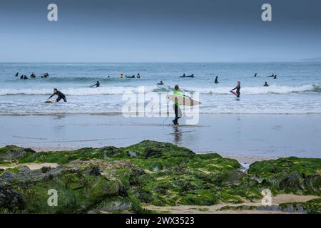 Eine Surferin, die nach dem Surfen am Towan Beach in Newquay in Cornwall in Großbritannien mit ihrem Surfbrett aus dem Meer ging. Stockfoto