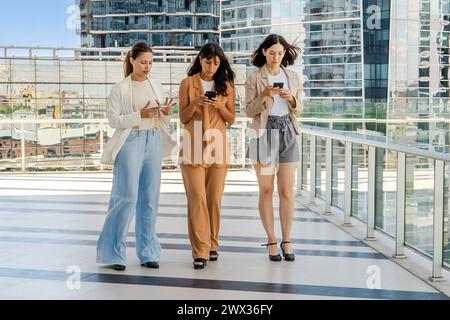 Drei Geschäftsfrauen laufen im Freien, während sie Smartphones benutzen. Alle Frauen sind in Geschäftskleidung gekleidet. Stockfoto