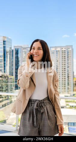 Eine lächelnde Unternehmerin benutzt ihr Smartphone, um sich mit jemandem zu unterhalten. Stockfoto