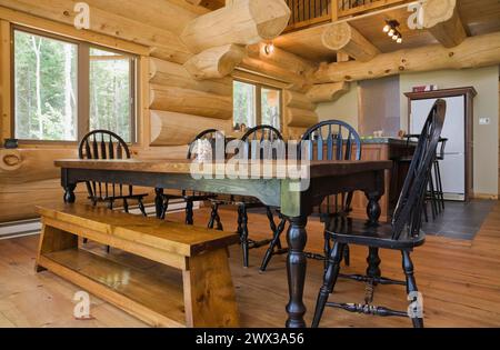 Esstisch aus schwarzem gebeiztem antikem Holz mit abgerundeten Stühlen mit hoher Rückenlehne und Sitzbank aus Kiefernholz im offenen Speisesaal und in der Küche Stockfoto