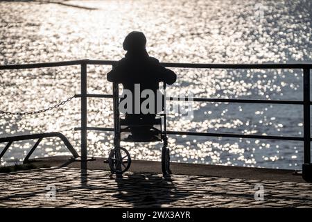 Ältere Dame, Seniorin, sitzt auf einem Rollator am Fluss und genießt die Sonne. Stockfoto