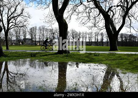 Edinburgh, Schottland, Großbritannien. März 2024. Überflutung rund um den Inverleith Park nach starken Regenfällen über Nacht bis in den frühen Nachmittag, schließlich durch Sonnenschein und einige Duschen. Jogger und Radfahrer vermeiden die Überschwemmungen im Inverleith Park. Quelle: Craig Brown/Alamy Live News Stockfoto