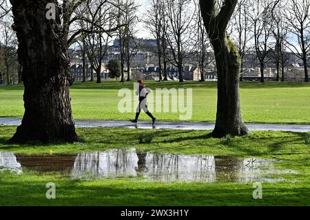 Edinburgh, Schottland, Großbritannien. März 2024. Überflutung rund um den Inverleith Park nach starken Regenfällen über Nacht bis in den frühen Nachmittag, schließlich durch Sonnenschein und einige Duschen. Jogger vermeidet die Überschwemmungen im Inverleith Park mit Blick auf das Schloss. Quelle: Craig Brown/Alamy Live News Stockfoto