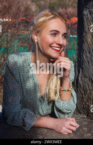 Eine junge Frau mit blonden Haaren und neugierigem Gesichtsausdruck steht vor einem alten Mauerbruch. Ihr luftiges Sommerkleid steht im Kontrast zum h Stockfoto