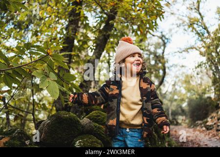 Porträt eines modischen kleinen Jungen mit Hut, der glücklich auf einem Waldweg spielt, während er seinen Eltern etwas über Pflanzen beibringt Stockfoto