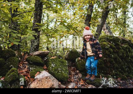 Porträt eines modischen kleinen Jungen mit Hut, der glücklich auf einem Waldweg spielt, während er seinen Eltern etwas über Pflanzen beibringt Stockfoto