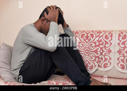 Ein Indianer sitzt allein auf einer Couch, mit dem Kopf in den Händen und vermittelt Gefühle der Traurigkeit und Verzweiflung. Stockfoto