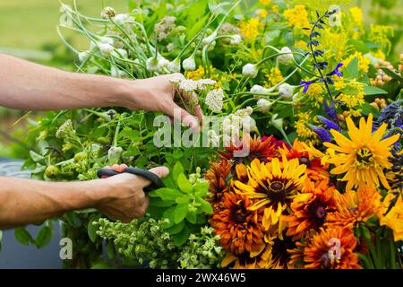 Ein Blumenhändler schneidet im Sommer wilde Blumen, während er im Freien ein Blumenarrangement anfertigt. Stockfoto