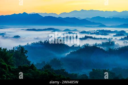 Der Herbstsonnenaufgang in einer hügeligen Stadt im Süden Taiwans ist eine nebelige Landschaft, in der das strahlende Sonnenlicht durch mehrschichtige Nebelschwaden hindurchzieht. Stockfoto