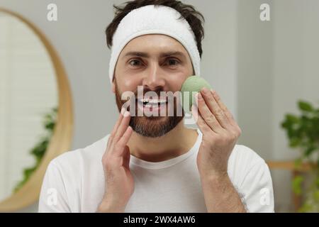 Mann mit Stirnband, der sein Gesicht mit Schwamm im Badezimmer wäscht Stockfoto