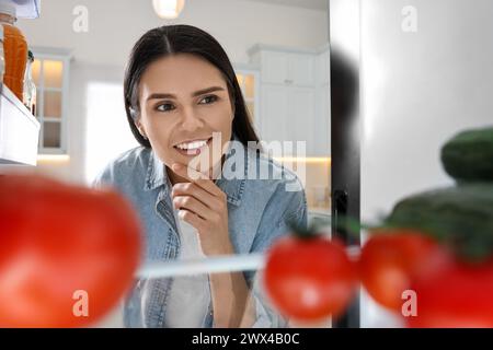Aufmerksame Frau in der Nähe des Kühlschranks in der Küche, Blick von innen Stockfoto