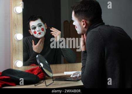 Junger Mann, der Mime in der Nähe des Spiegels in der Garderobe schminkt Stockfoto