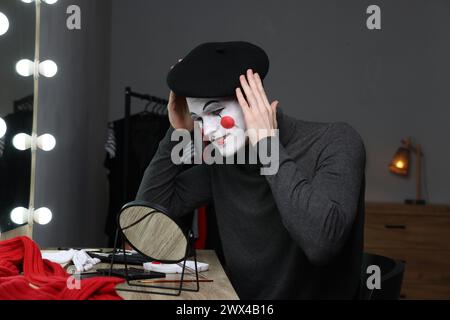 MIME-Künstler, der Baskenmütze in der Nähe des Spiegels in der Garderobe auflegt Stockfoto