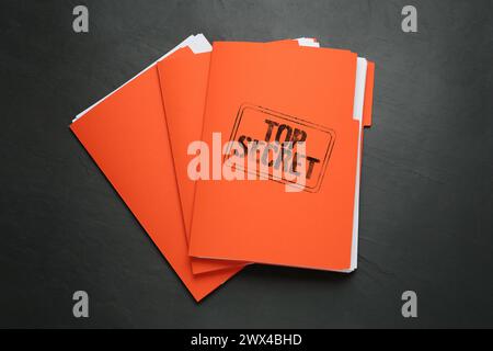 Streng geheimer Stempel. Orangefarbene Dateien mit Dokumenten auf schwarzer Tabelle, Draufsicht Stockfoto