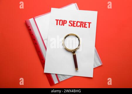 Streng geheimer Stempel. Lupe, Blatt Papier und Ordner auf rotem Hintergrund, Draufsicht Stockfoto