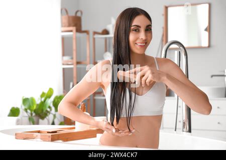 Schöne junge Frau mit Kokosöl, die Haare im Badezimmer kämmt Stockfoto