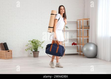 Sportliche junge Frau mit Tasche und Yogamatte im Fitnessstudio Stockfoto