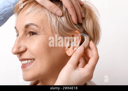 Junge Frau, die Hörgerät in das Ohr reifer Frau auf weißem Hintergrund legt, Nahaufnahme Stockfoto