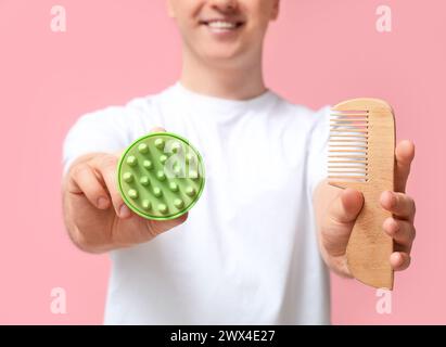 Junger Mann mit Haarkopf-Massagegerät und Kamm auf rosafarbenem Hintergrund Stockfoto