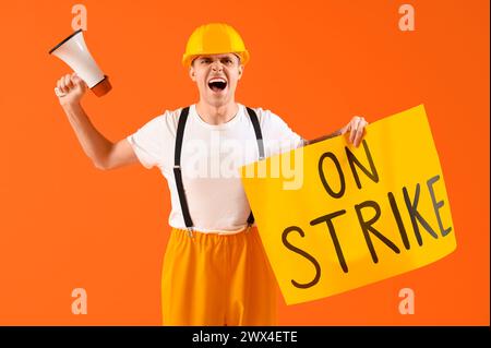 Protest gegen die Feuerwehr mit Plakat mit STREIKTEXT und Megaphon vor orangem Hintergrund Stockfoto
