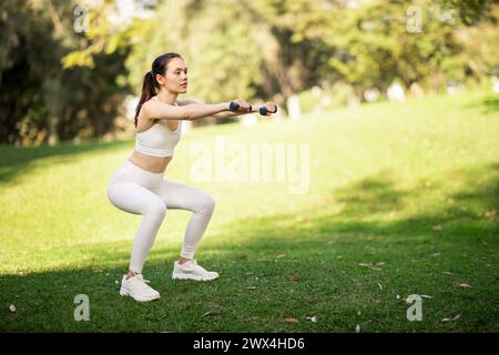 Entschlossene Frau, die im Freien mit Handgewichten hockt Stockfoto