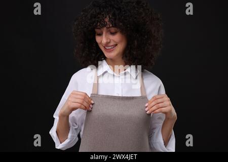 Glückliche Frau, die Küchenschürze auf schwarzem Hintergrund trägt. Modell für Design Stockfoto