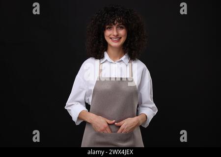 Glückliche Frau, die Küchenschürze auf schwarzem Hintergrund trägt. Modell für Design Stockfoto