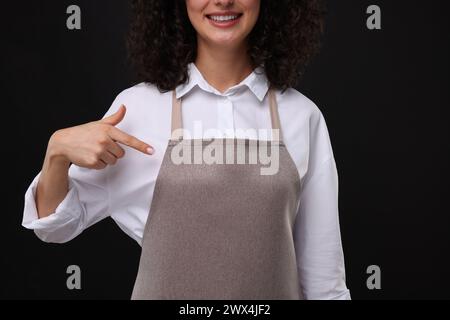 Frau, die auf Küchenschürze auf schwarzem Hintergrund zeigt, Nahaufnahme. Modell für Design Stockfoto