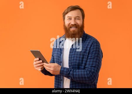 Fröhlicher rothaariger bärtiger Mann in zwangloser Hand mit digitalem Tablet, Studio Stockfoto