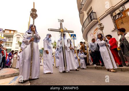 Almuneca, Spanien. Die Osterwoche in Almuneca, Spanien, beginnt mit dem ersten großen Ereignis, dem Palmensonntag (Domingo de Ramos), dem Feiertag, der genau eine Woche vor dem Ostersonntag stattfindet und an Jesu berühmten Einzug auf einem Esel in Jerusalem erinnert. Die Bruderschaften organisieren die Prozessionen, die jeden Tag durch die Straßen und Plätze ziehen, mit wunderschönen „Pasos“ und „Tronos“, die mit Blumen und religiösen Bildern geschmückt sind, die auf den Schultern der Teilnehmer getragen werden. Hier tragen die Kinder der Kirche ein großes Kreuz und Kerzen bei der Parade durch Almuñécar. März 2024 David Smith/Alamy Stockfoto