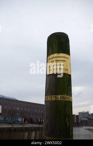 Husum, Schleswig-Holstein Sturmflutpfahl am Ende des Hafenbeckens, der Hafenspitze des Husumer Binnenhafens. Der Pfahl zeigt die Wasserstände nach den wuchtigen Fluten an, die Ort maßgeblich prägten und prägen. Am oberen Ende sieht man die Wasserhöhe NN null am Sperrwerk. Ca. 60 cm darunter die Marke der Sturmflut von 1976 usw. Aufnahme vom 27.03.2024, Husum, Kreis Nordfriesland, Schleswig-Holstein *** Husum, Schleswig-Holstein Sturmflut am Ende des Hafenbeckens, der Hafenspitze des Husumer Binnenhafens der Haufen zeigt die Wasserstände nach den massivsten Überschwemmungen an, die signalisieren Stockfoto