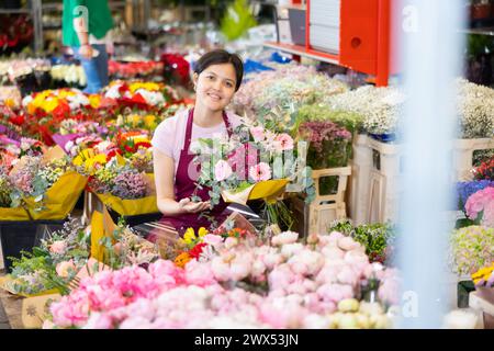 Asiatische Blumenläuferin, die im Blumengeschäft Blumenstrauß mit Rosen und Gerberas zubereitet Stockfoto