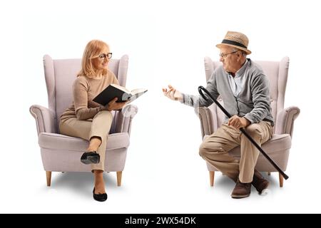 Ein älterer Mann spricht mit einer Frau, die in einem Sessel sitzt und ein Buch auf weißem Hintergrund hält Stockfoto