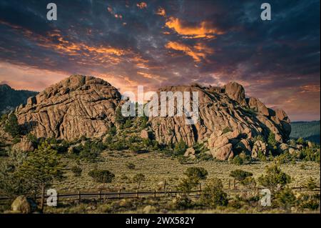 Dramatische Wolken färben den Himmel, während der Sonnenuntergang ein warmes Leuchten über eine beeindruckende Felsformation wirft Stockfoto