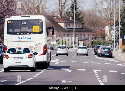 Haguenau, Frankreich - 20. März 2024: Eine belebte Straße in Haguenau zeigt einen Schulbus und Autos, die entlang der Straße fahren. Stockfoto