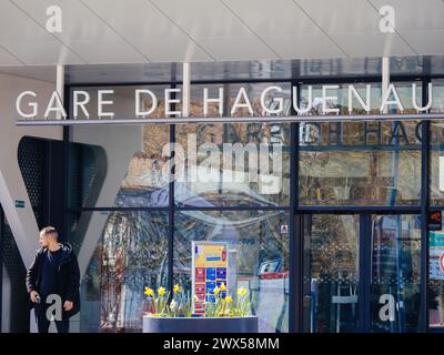 Haguenau, Frankreich - 20. März 2024: Eine männliche Figur steht am Eingang des Gare du Haguenau, mit blühenden Narzissenblüten in der Umgebung, die der städtischen Szene einen Hauch natürlicher Schönheit verleihen Stockfoto