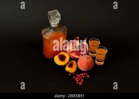 Granatapfelpfirsichlikör, hausgemachter Alkohol in zwei Gläsern und eine Flasche auf schwarzem Hintergrund, reife Früchte sind in der Nähe. Nahaufnahme. Stockfoto