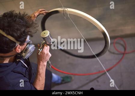 Person, die in seiner Werkstatt eine Schutzmaske trägt und eine Fahrradfelge lackiert. Hochwinkelansicht. Echte Menschen arbeiten. Stockfoto