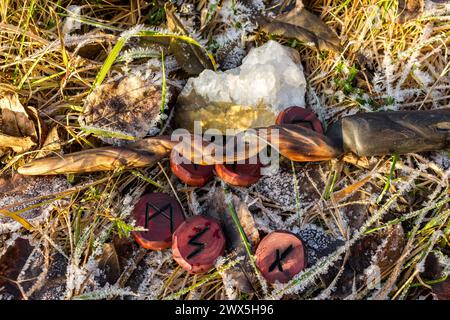 Skandinavische Runen und ein Zauberstab auf dem mit Raureif bedeckten Gras Stockfoto