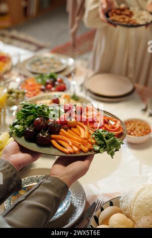 Vertikale Hochwinkelaufnahme der Hände nicht erkennbarer muslimischer Frauen, die einen festlichen Tisch für Eid Al-Fitr feiern Stockfoto