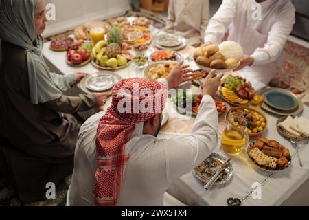 Blick aus einem hohen Winkel auf den jungen muslimischen Mann, der beim festlichen Abendessen auf Uraza Bayram mit seiner Familie Essen teilt Stockfoto